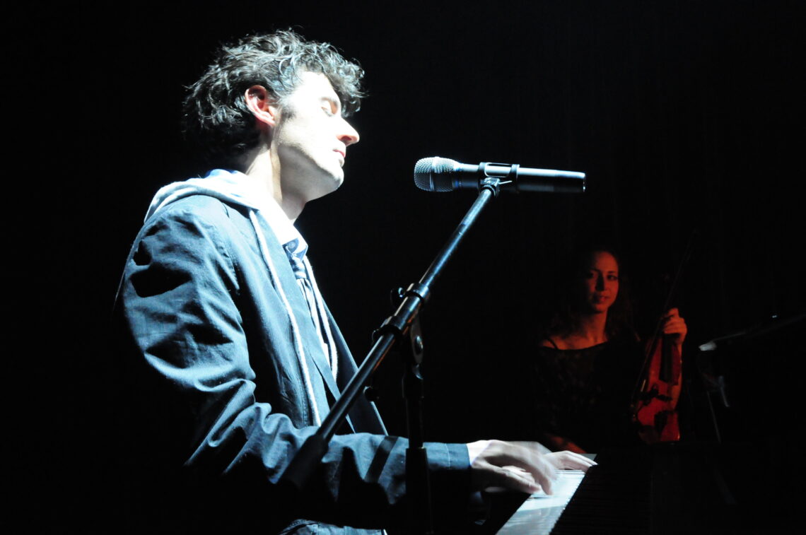 Roger Stein singt im Scheinwerferlicht am Keyboard, im Hintergrund eine Geigerin