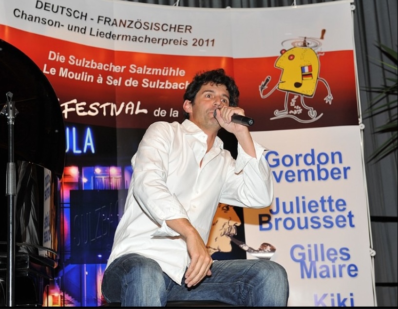 Roger Stein mit Mikrofon vor dem Banner des Deutsch-Französischen Chanson- und Liedermacherpreises 2011