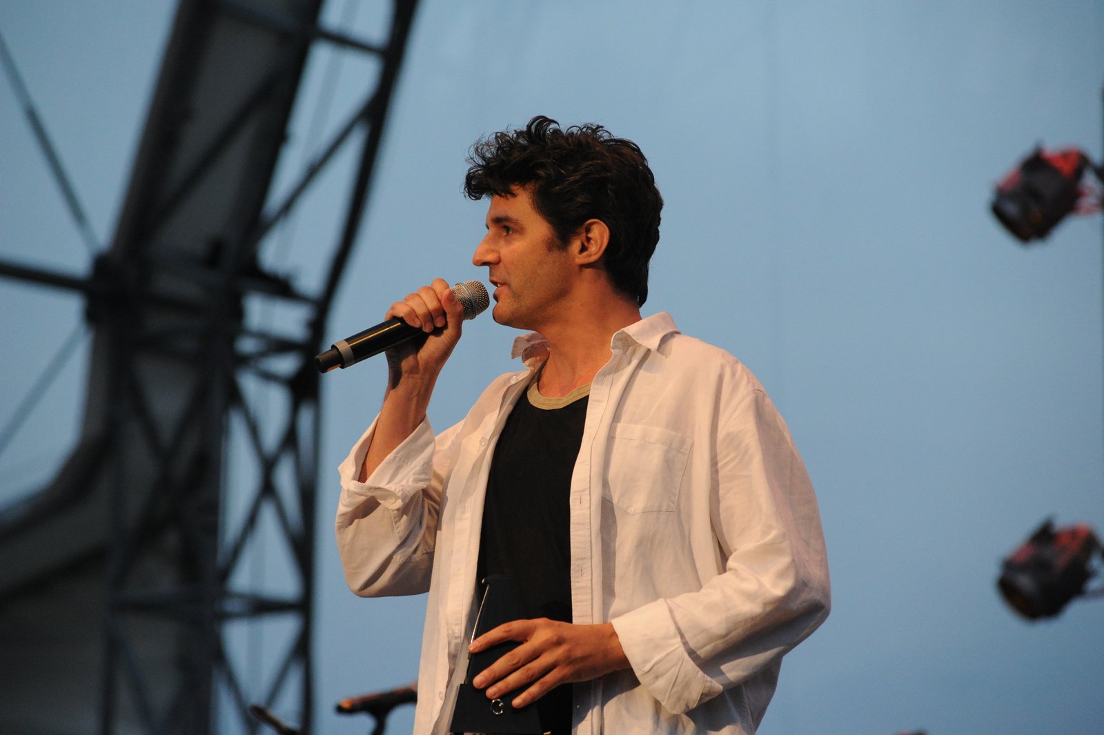 Roger Stein spricht mit Mikrofon auf einer Open-Air-Bühne und hält eine Trophäe in der Hand