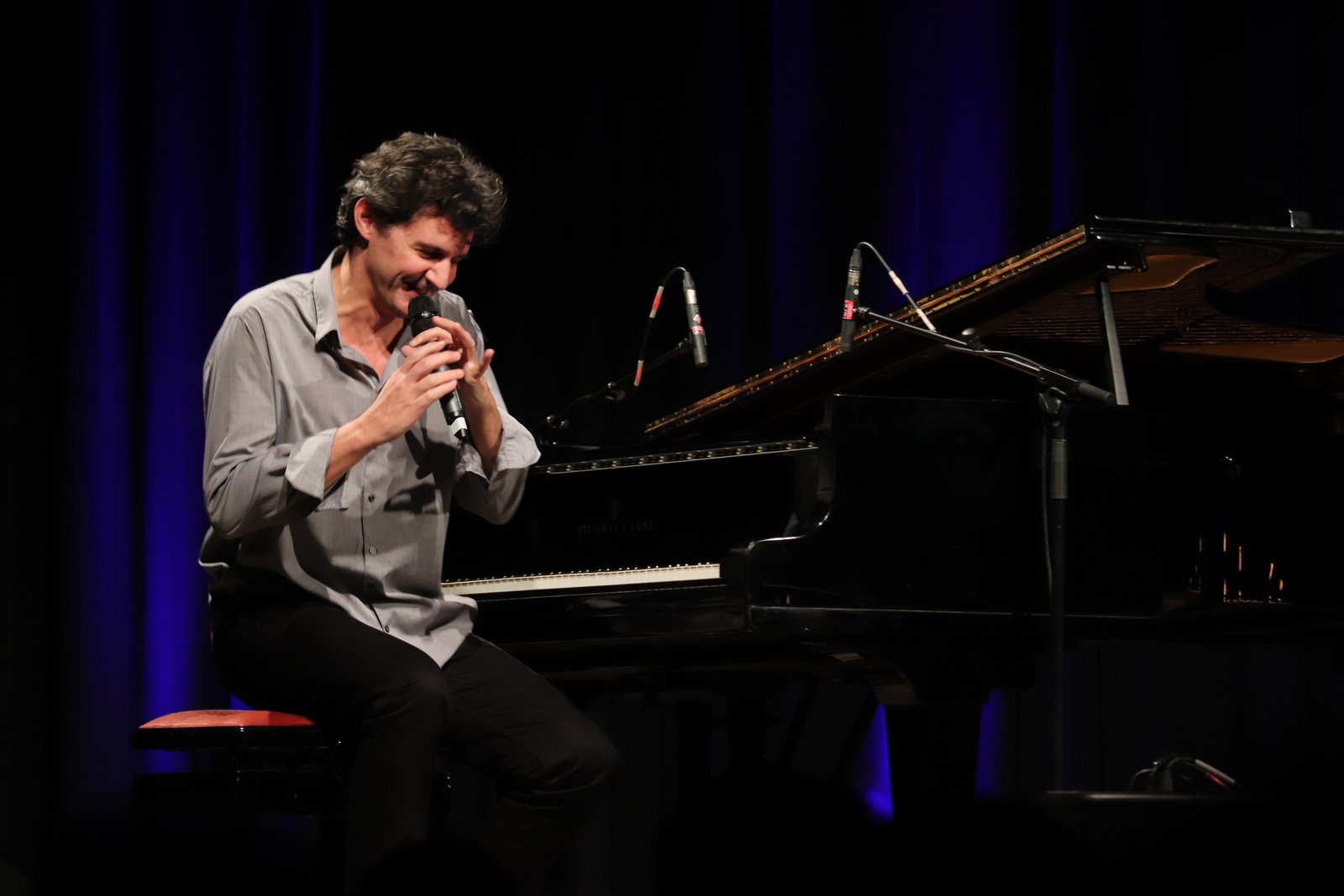Roger Stein sitzt lachend am Flügel und singt ins Mikrofon