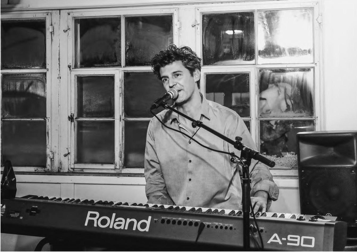 Schwarz-Weiß-Foto: Roger Stein singt am Keyboard vor alten Sprossenfenstern