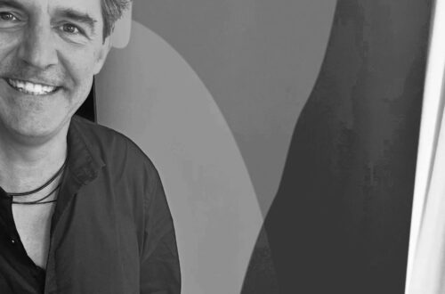 Roger Stein lächelnd vor dem Banner von Deutschlandfunk Kultur im Funkhaus Berlin, Schwarzweissfoto